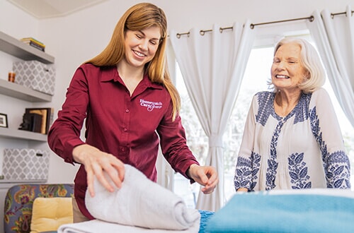 Homewatch caregiver helping lady with folding white bath towel